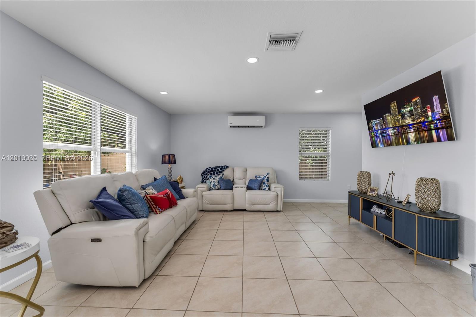 A living room features light tile flooring, two white sofas, and a wall-mounted television — HOMESTEAD, FL