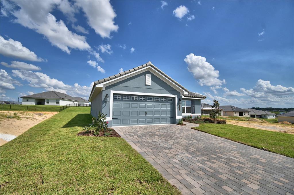 A blue single-story house with a two-car garage and a paved driveway under a cloudy sky — 5427 WATERSIDE DRIVE, AUBURNDALE, FL