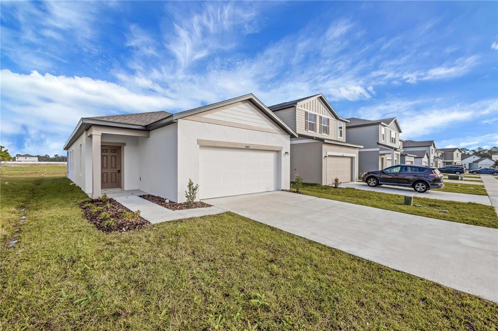 A single-story house with a white stucco exterior, a two-car garage, and a concrete driveway — 35605 BUTTONWEED TRAIL, ZEPHYRHILLS, FL