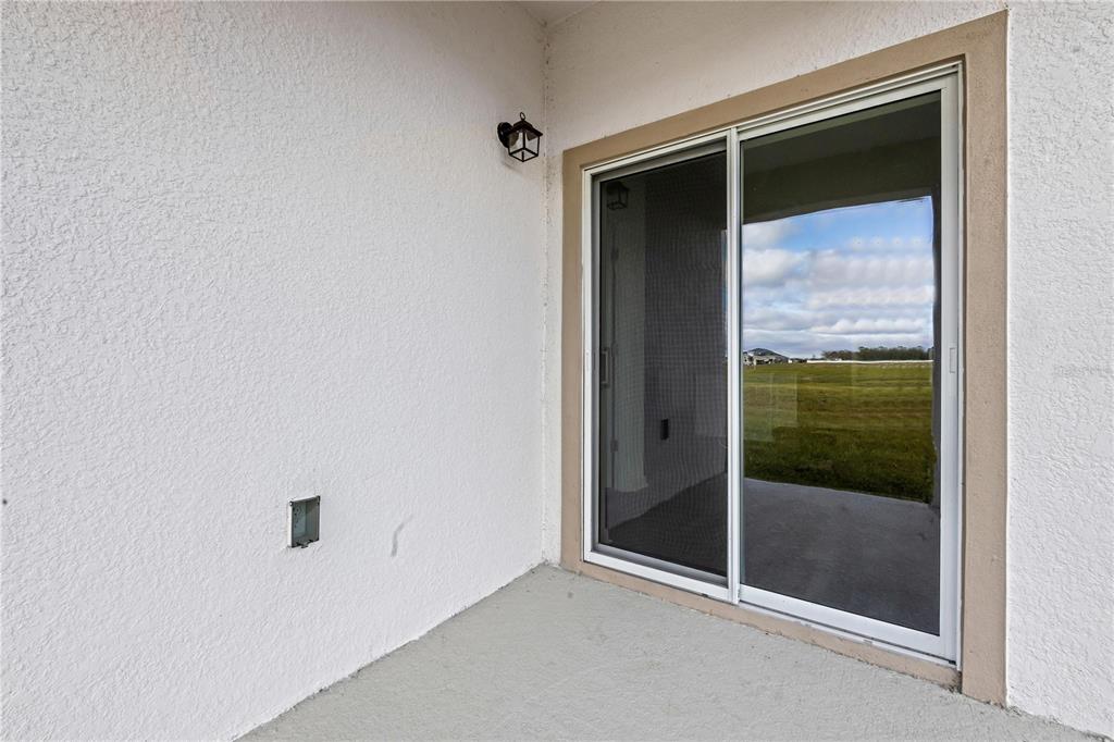 A covered patio features a white stucco wall, a sliding glass door, and an outdoor light — 35605 BUTTONWEED TRAIL, ZEPHYRHILLS, FL