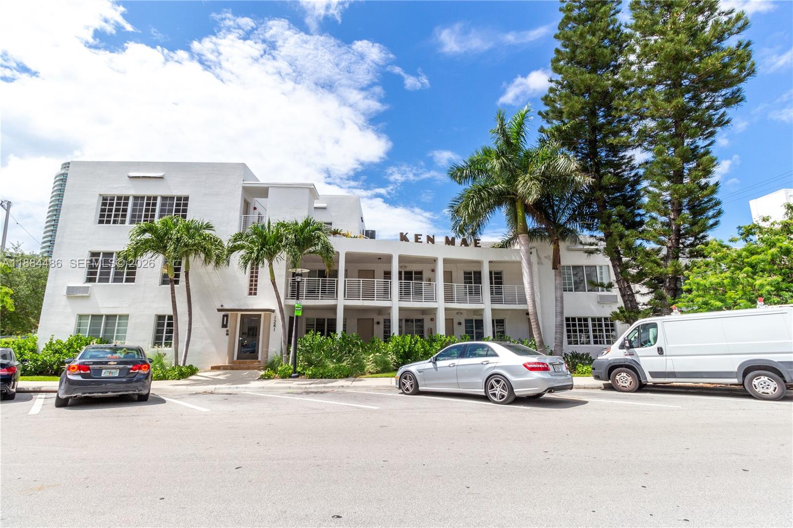 The exterior of a white multi-story apartment building features palm trees and a parking lot — 1241 14th St # 9, Miami Beach FL 33139, MIAMI BEACH, FL