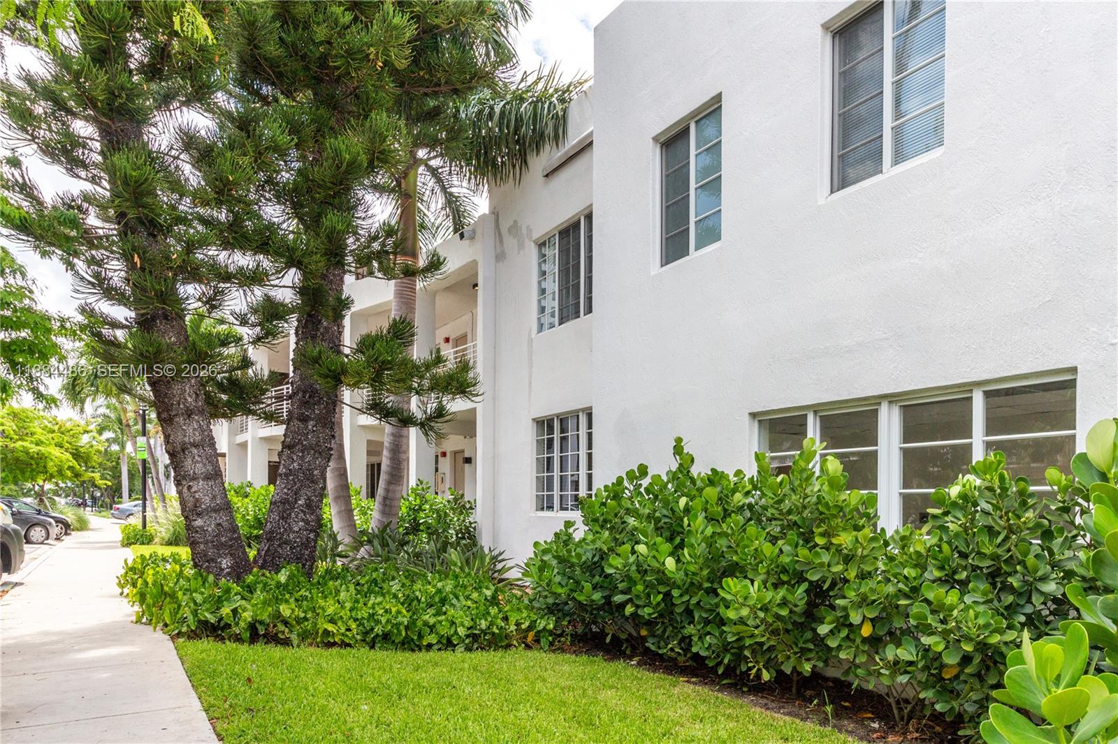 The exterior of a white multi-story building features palm trees, a glass door, and balconies — 1241 14th St # 9, Miami Beach FL 33139, MIAMI BEACH, FL