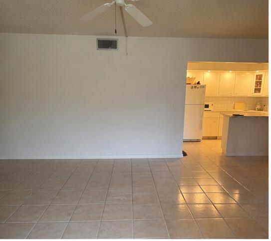 An empty room with light-colored tile flooring leads into a kitchen with white cabinets — 409 Pine Glen Lane # 1, FL 33463, FL