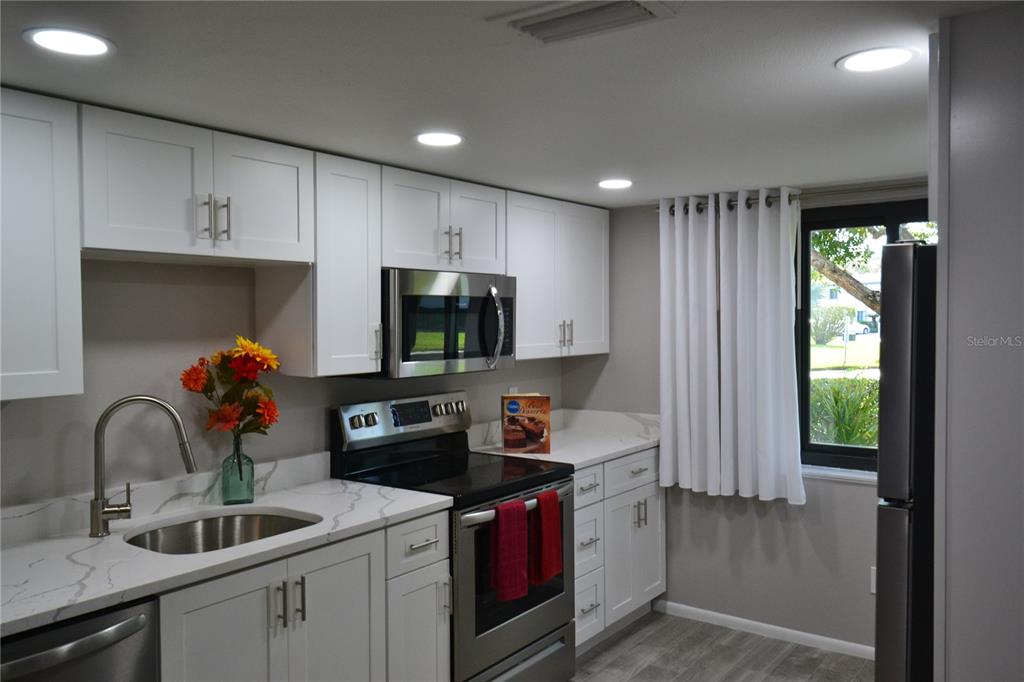 A modern kitchen features white cabinets, stainless steel appliances, and white marble-look countertops — 135 W CYPRESS COURT, OLDSMAR, FL