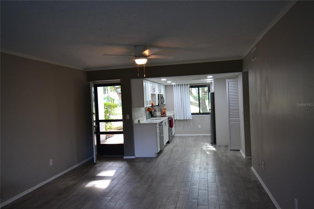 A living room with gray wood-look flooring leads to an open kitchen with white cabinets — 135 W CYPRESS COURT, OLDSMAR, FL