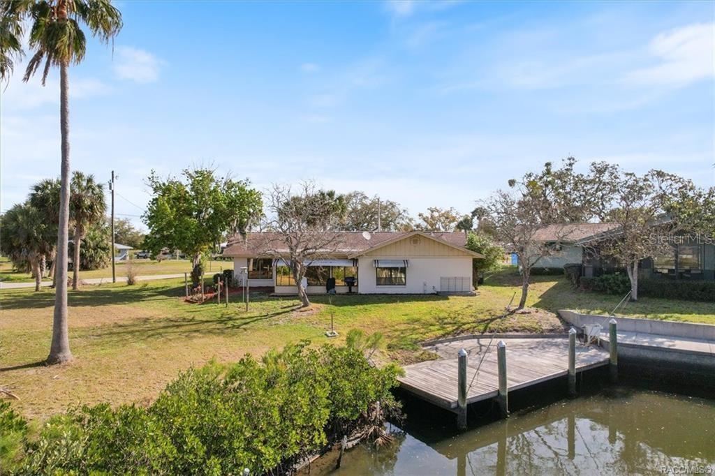 A single-story house with a wooden dock sits along a canal under a blue sky — 11684 W SUNNYBROOK COURT, CRYSTAL RIVER, FL
