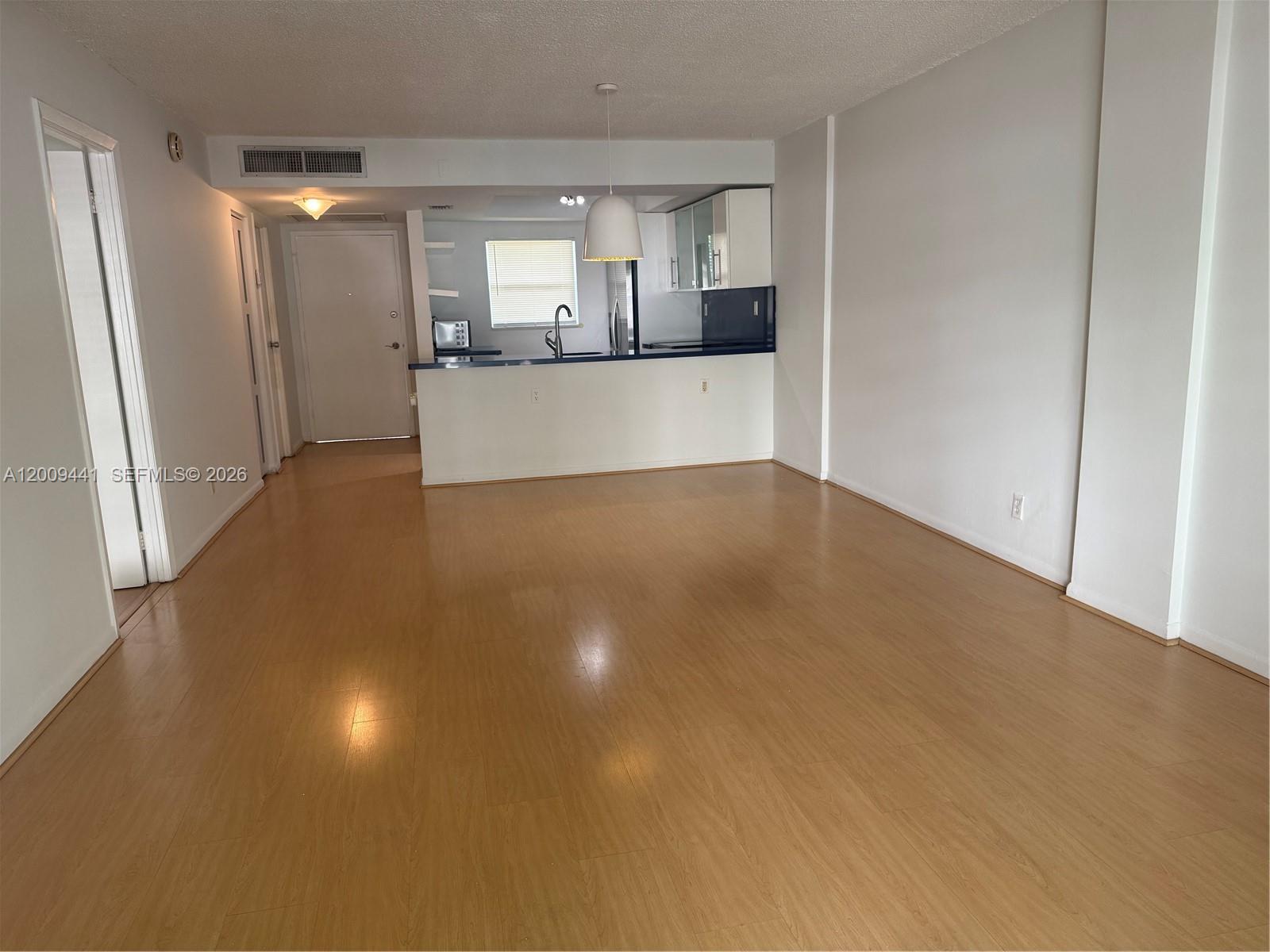 An open-plan living area features light wood flooring, white walls, and a kitchen with a breakfast bar — 100 Edgewater Dr # 236, Coral Gables FL 33133, CORAL GABLES, FL