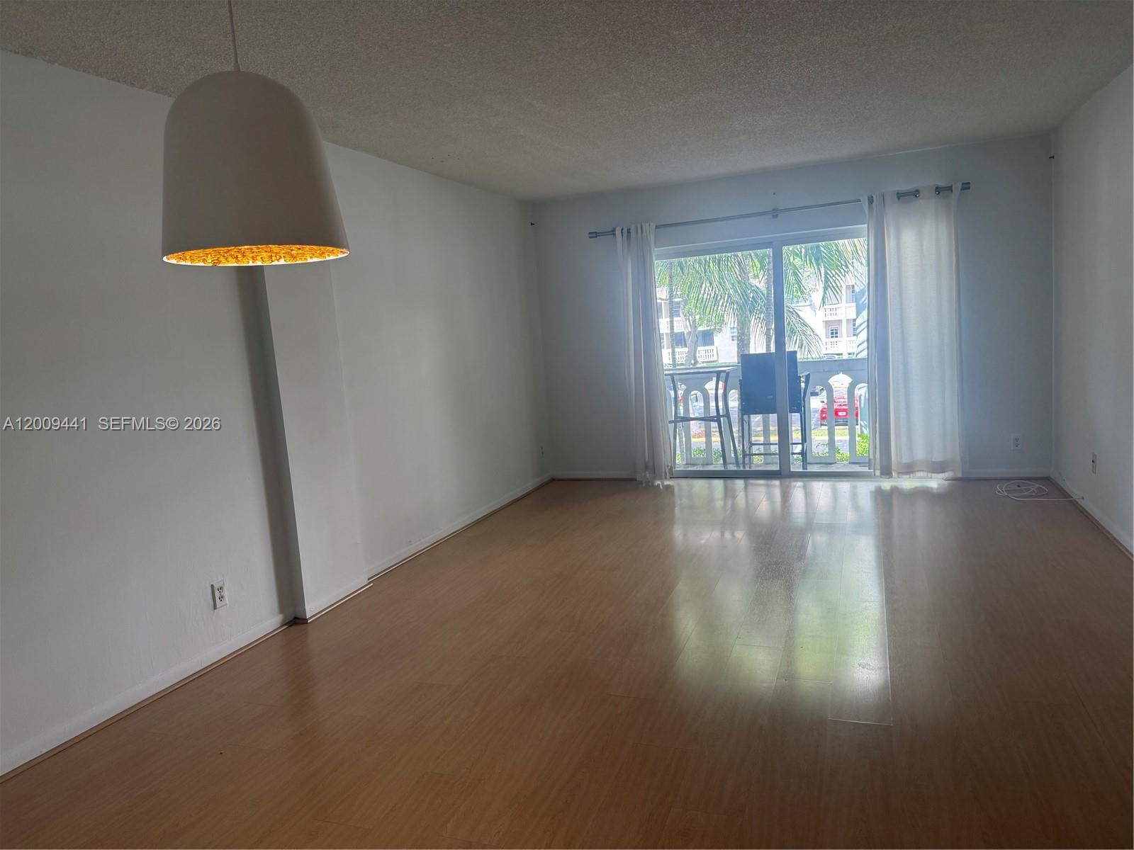 An empty living room features light wood flooring, white walls, and a sliding glass balcony door — 100 Edgewater Dr # 236, Coral Gables FL 33133, CORAL GABLES, FL