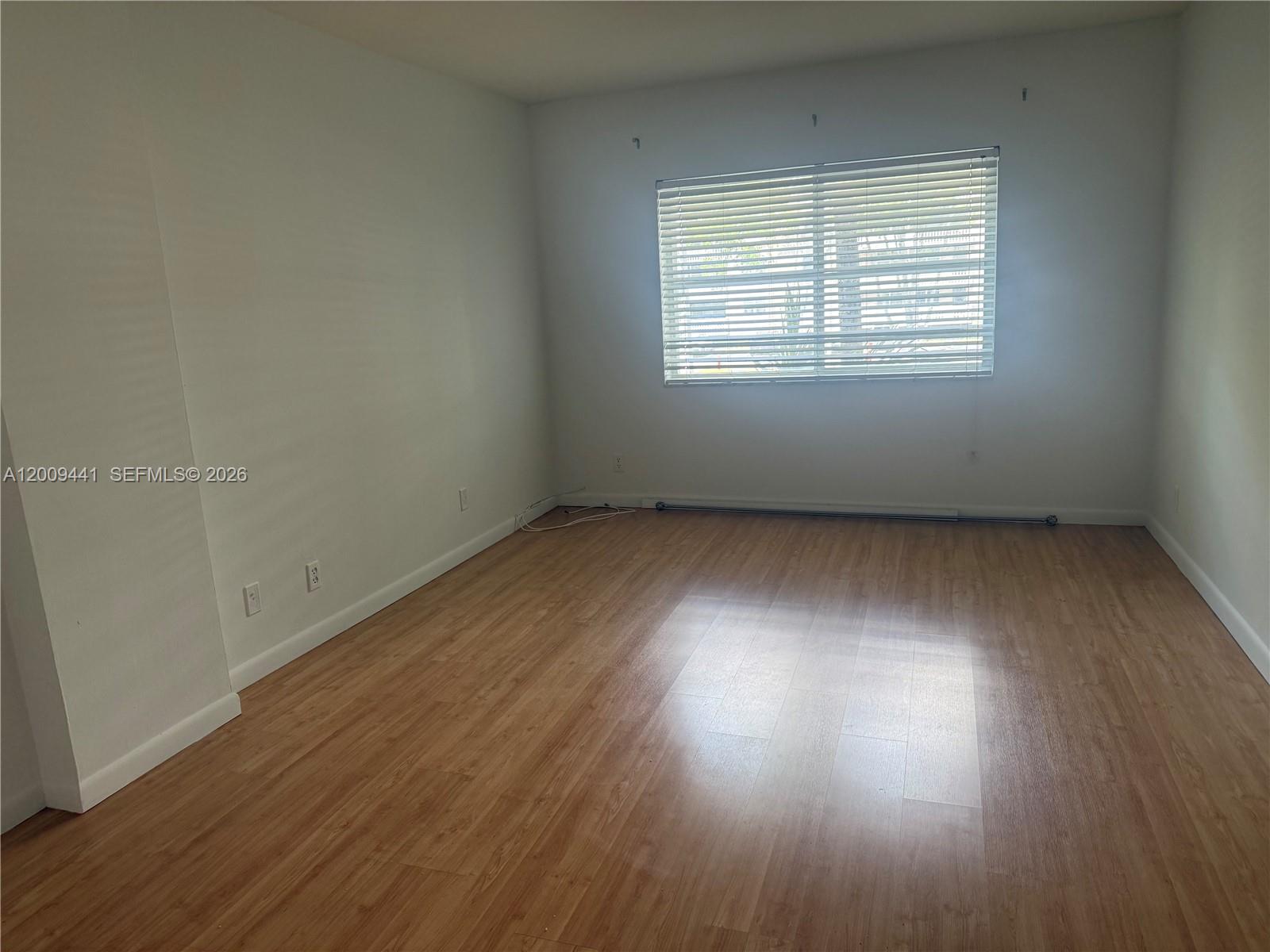 An empty room with light wood-look flooring, white walls, and a window with blinds — 100 Edgewater Dr # 236, Coral Gables FL 33133, CORAL GABLES, FL