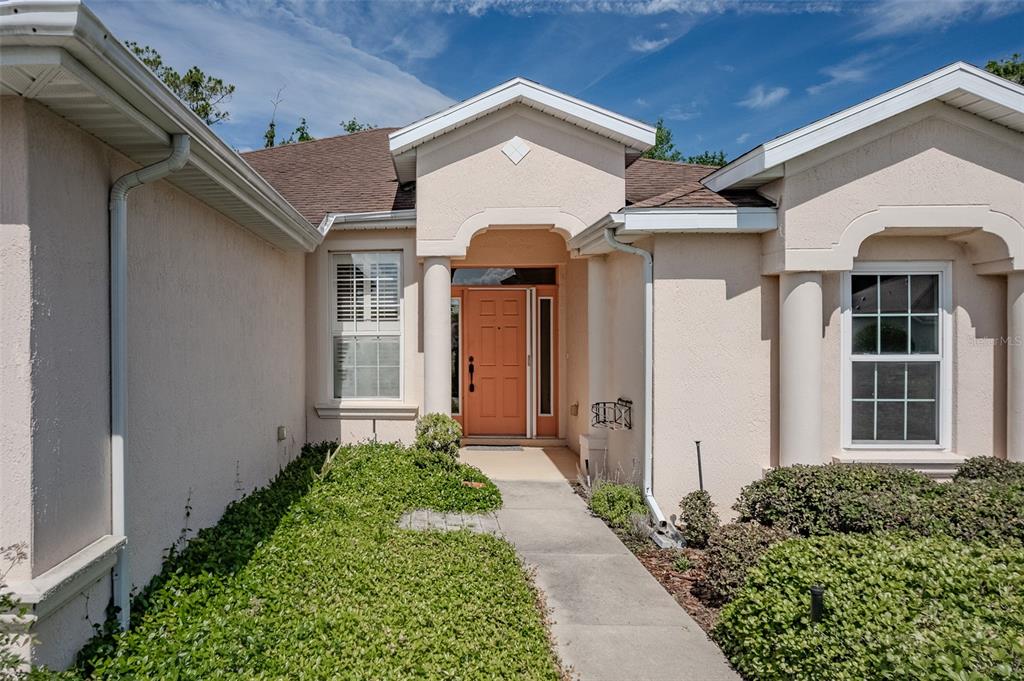 The exterior of a beige stucco house features a covered entryway with columns and an orange door — 1520 SW 152ND PLACE, OCALA, FL