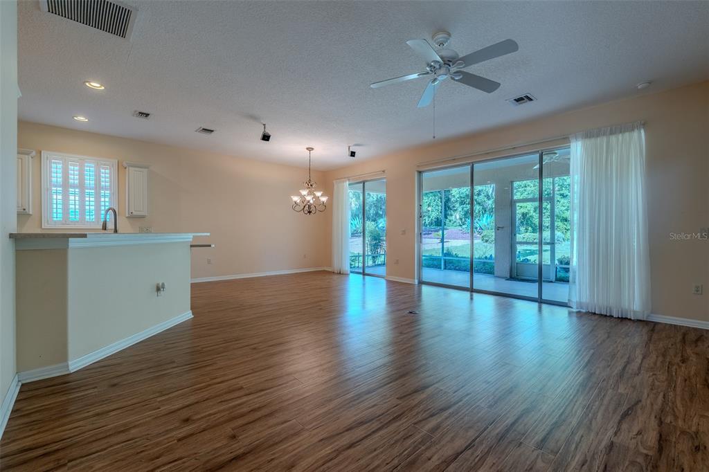 An open-concept living area features wood-look flooring, a kitchen island, and sliding glass patio doors — 1520 SW 152ND PLACE, OCALA, FL