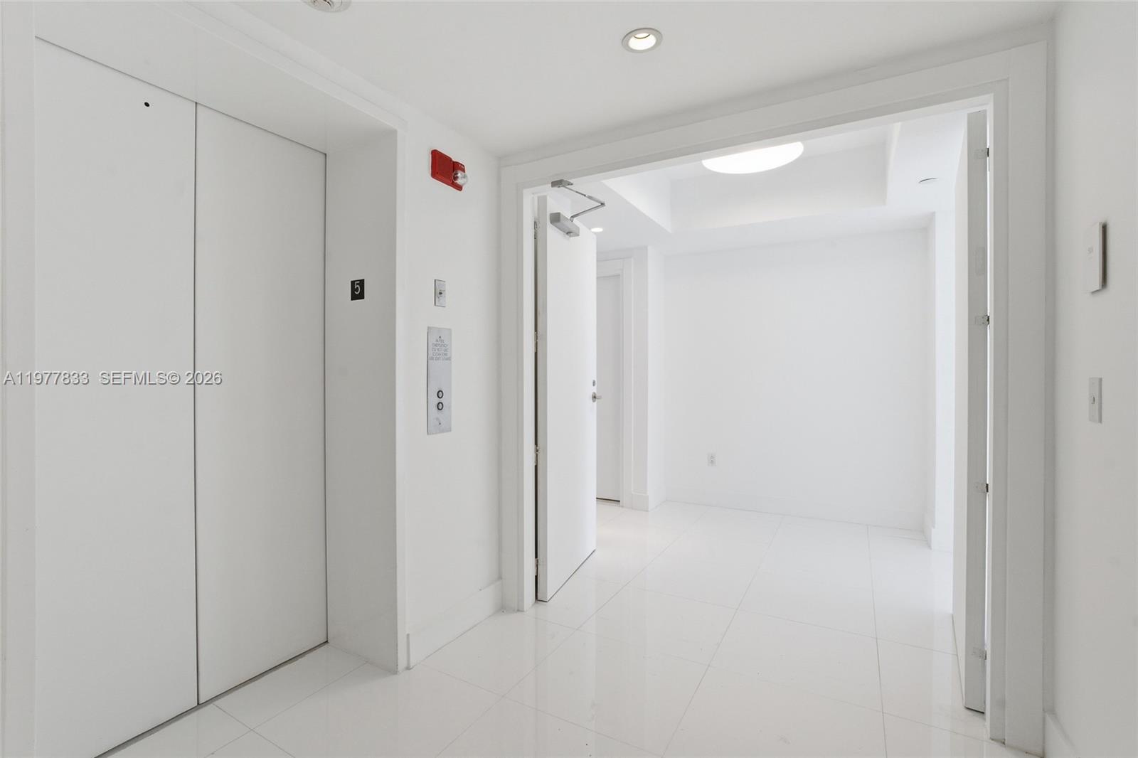 A bright, white-tiled hallway features an elevator door and an open doorway leading to a room — 2627 S Bayshore Dr # 501, Miami FL 33133, MIAMI, FL