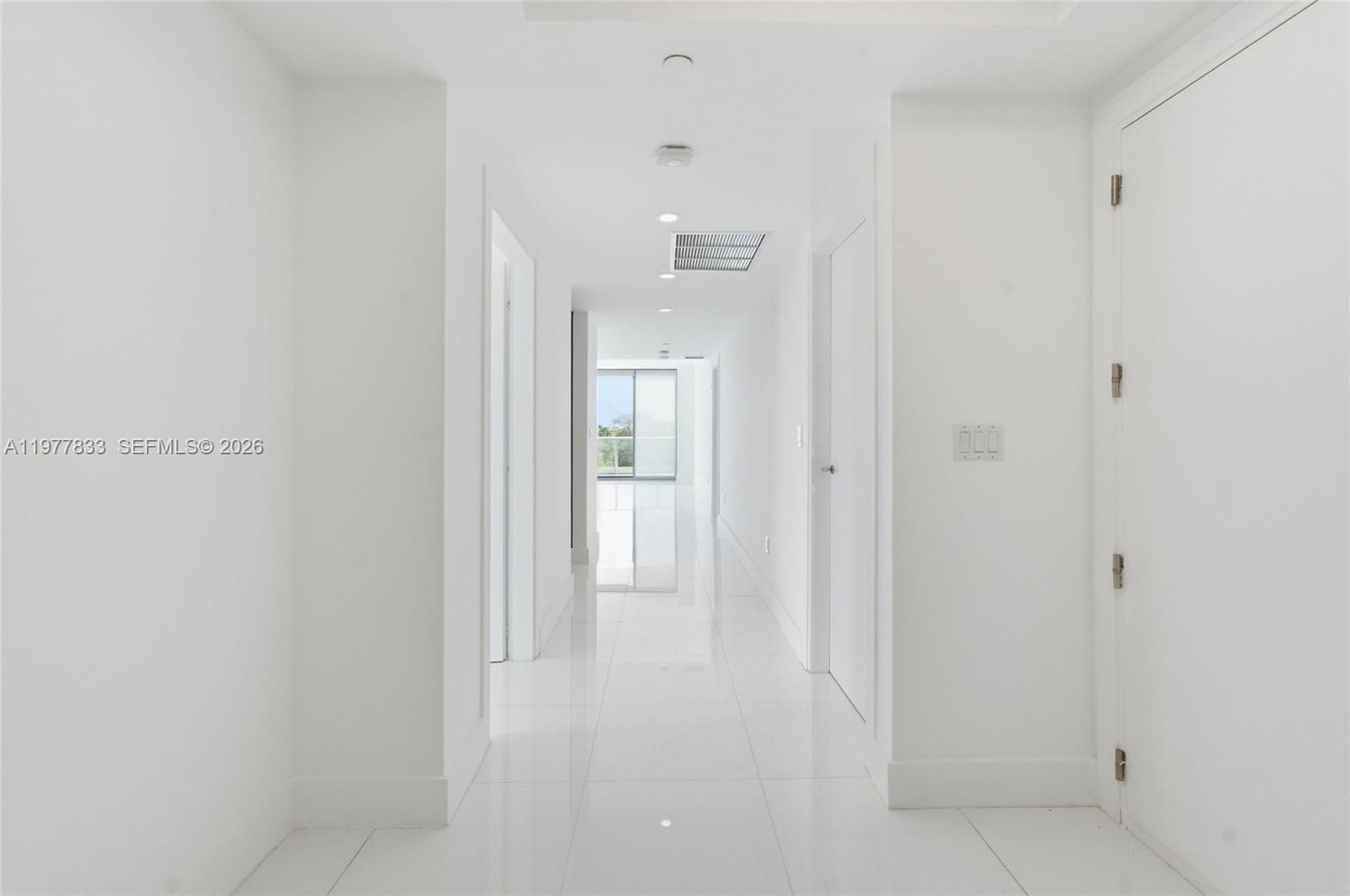 A bright, minimalist hallway features white walls, glossy tile flooring, and several closed doors — 2627 S Bayshore Dr # 501, Miami FL 33133, MIAMI, FL
