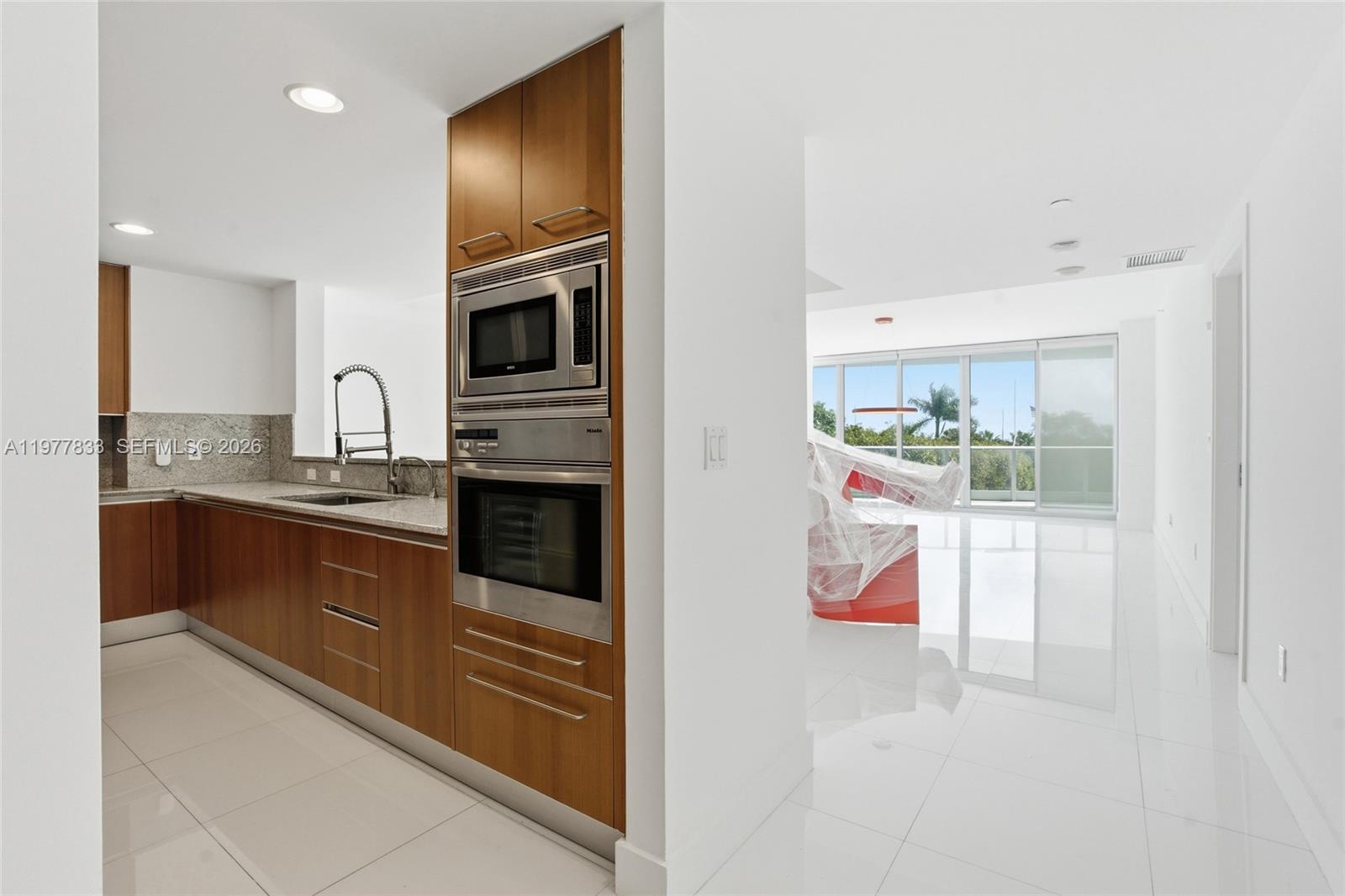 A kitchen with wood cabinetry and stainless steel appliances opens into a bright living area — 2627 S Bayshore Dr # 501, Miami FL 33133, MIAMI, FL