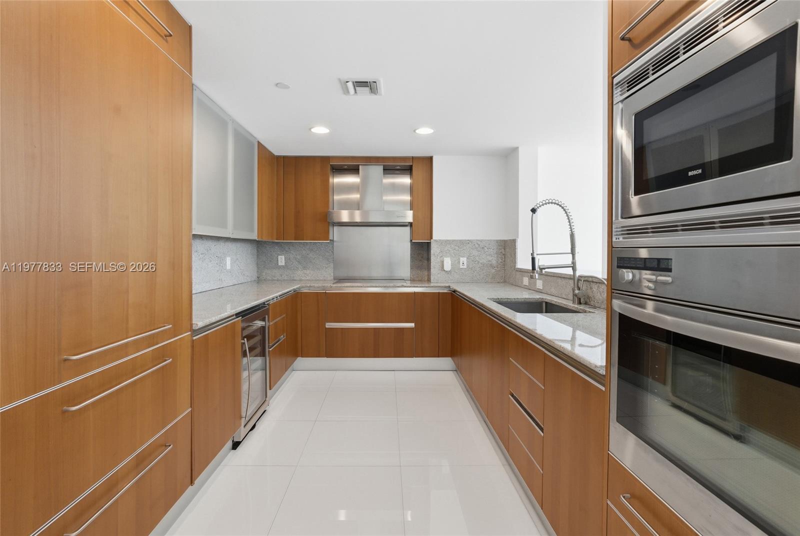 A modern kitchen features wood cabinetry, stainless steel appliances, and light-colored granite countertops — 2627 S Bayshore Dr # 501, Miami FL 33133, MIAMI, FL