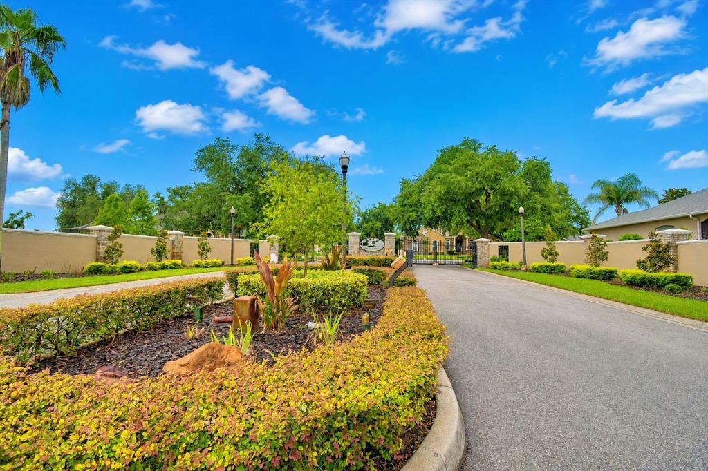 A paved driveway leads to a gated entrance with stone pillars and lush landscaping — 5516 BLACK HAWK LANE, LAKELAND, FL