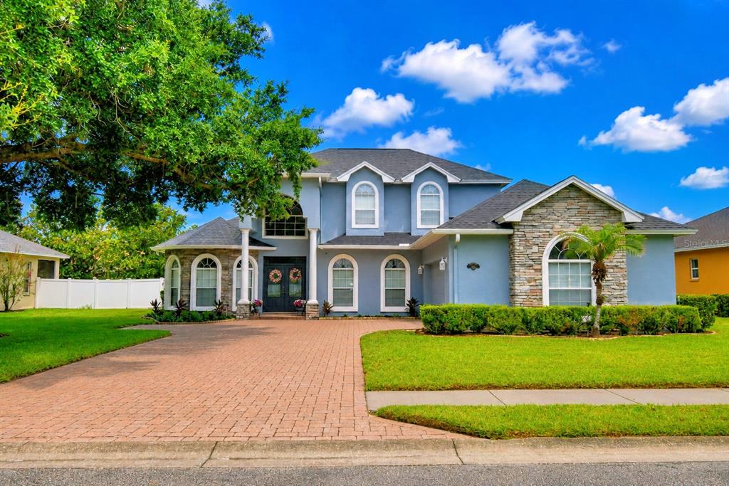 A two-story blue house with a stone facade, arched windows, and a brick driveway — 5516 BLACK HAWK LANE, LAKELAND, FL