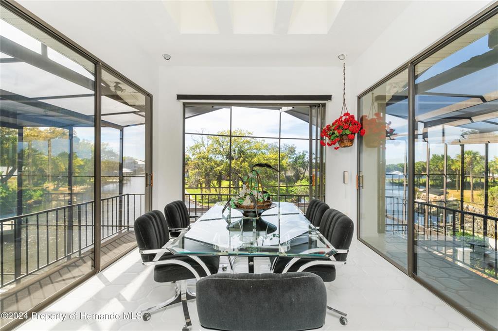 A dining room features a glass table, black chairs, and floor-to-ceiling windows overlooking water — 11915 W RIVERHAVEN DRIVE, HOMOSASSA, FL