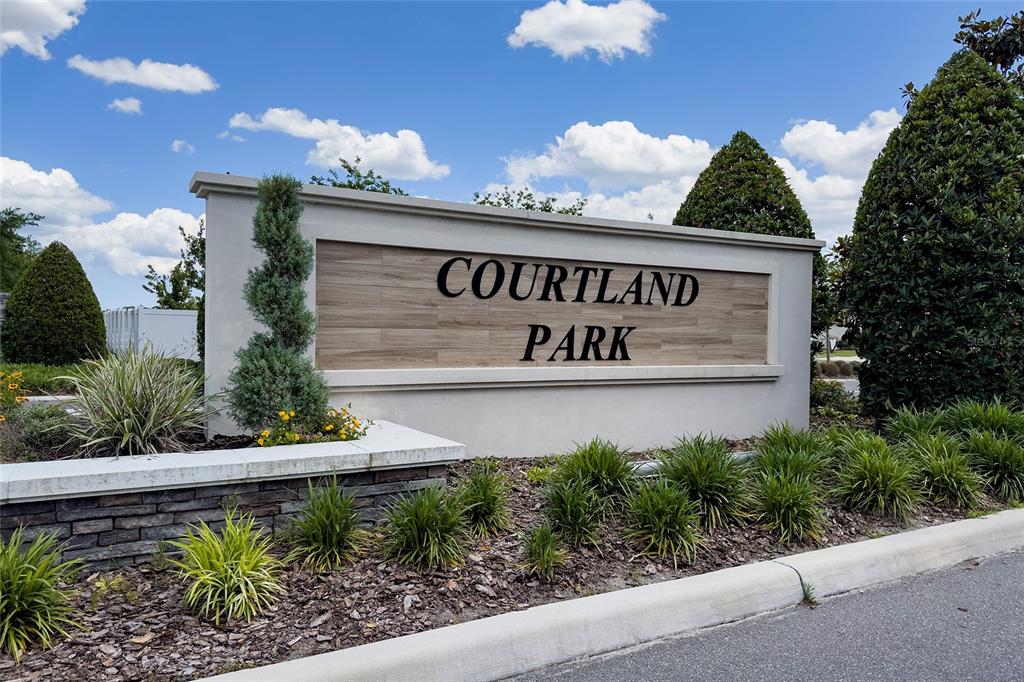 A stone and stucco monument sign for Courtland Park stands in a landscaped garden area — 928 AUGUST SKY DRIVE, DELTONA, FL