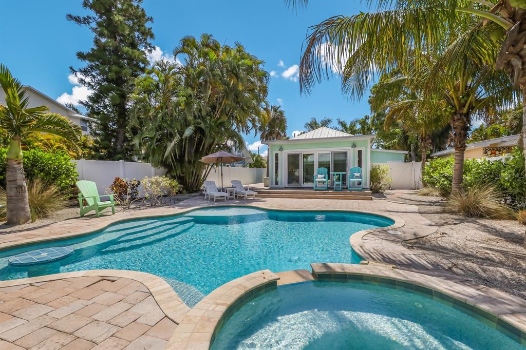 A backyard swimming pool and hot tub sit in front of a light green cottage — 504 SPRING AVENUE, ANNA MARIA, FL