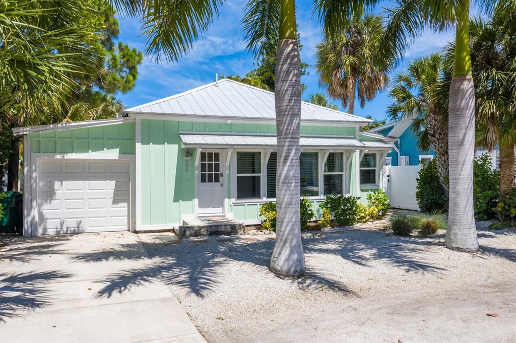 A light green cottage with a metal roof, white garage door, and palm trees outside — 504 SPRING AVENUE, ANNA MARIA, FL