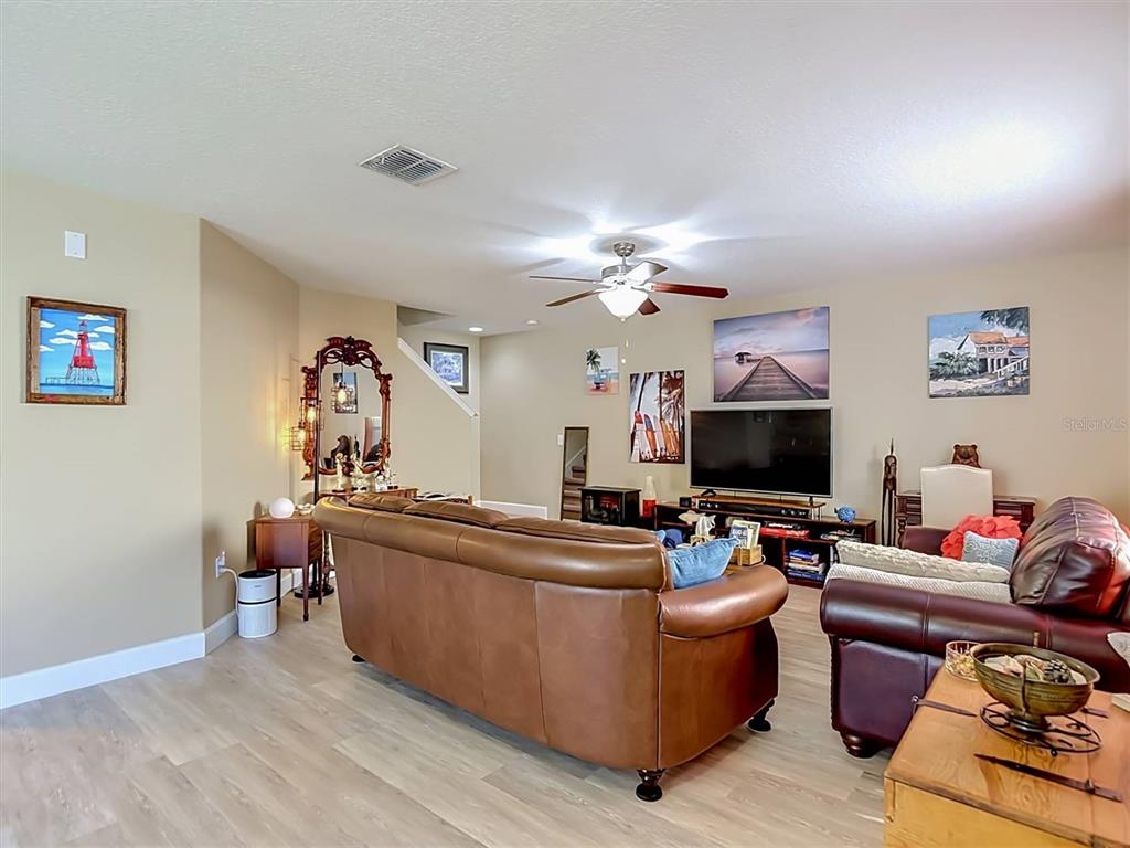A living room features a brown leather sofa, a television, and several wall art pieces — 9838 TRUMPET VINE LOOP, TRINITY, FL