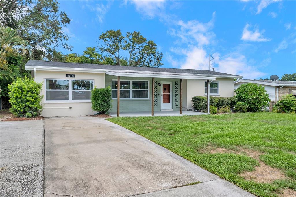 A single-story house with a concrete driveway, a covered porch, and light-colored brick siding — 1515 BELLEAIR RD, CLEARWATER, FL