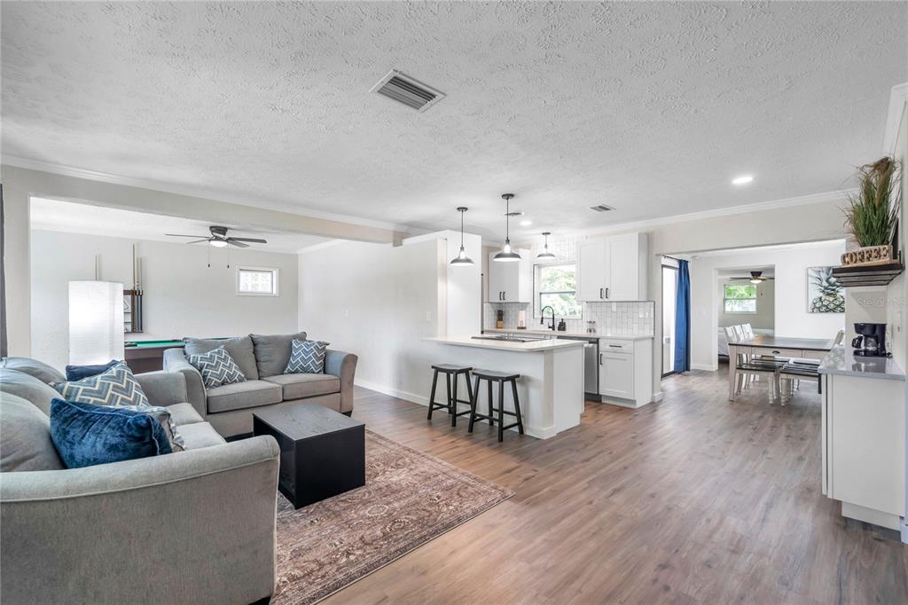 An open-concept living room and kitchen feature gray sofas, white cabinetry, and wood-look flooring — 1515 BELLEAIR RD, CLEARWATER, FL