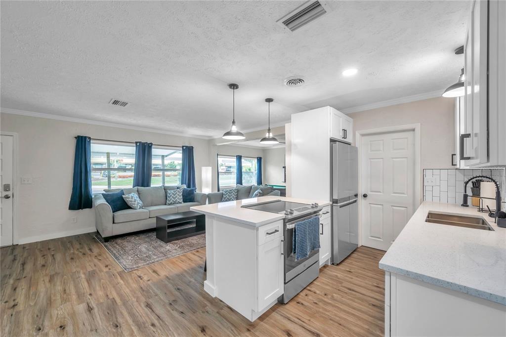 A kitchen with a white island and stainless steel appliances overlooks a living room area — 1515 BELLEAIR RD, CLEARWATER, FL