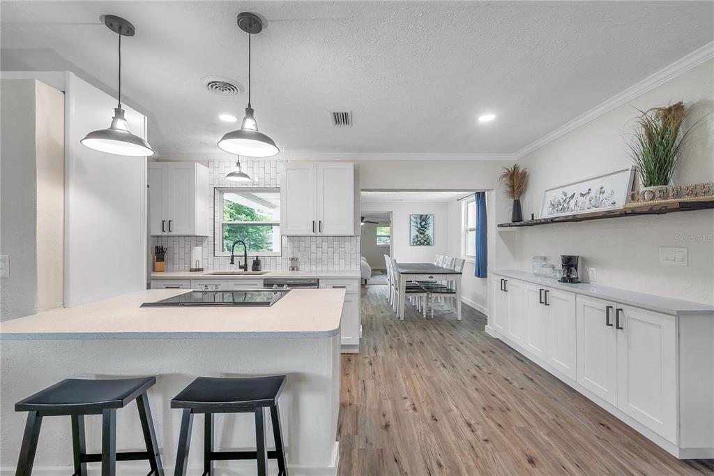 A white kitchen with a center island, pendant lighting, and wood-look flooring — 1515 BELLEAIR RD, CLEARWATER, FL