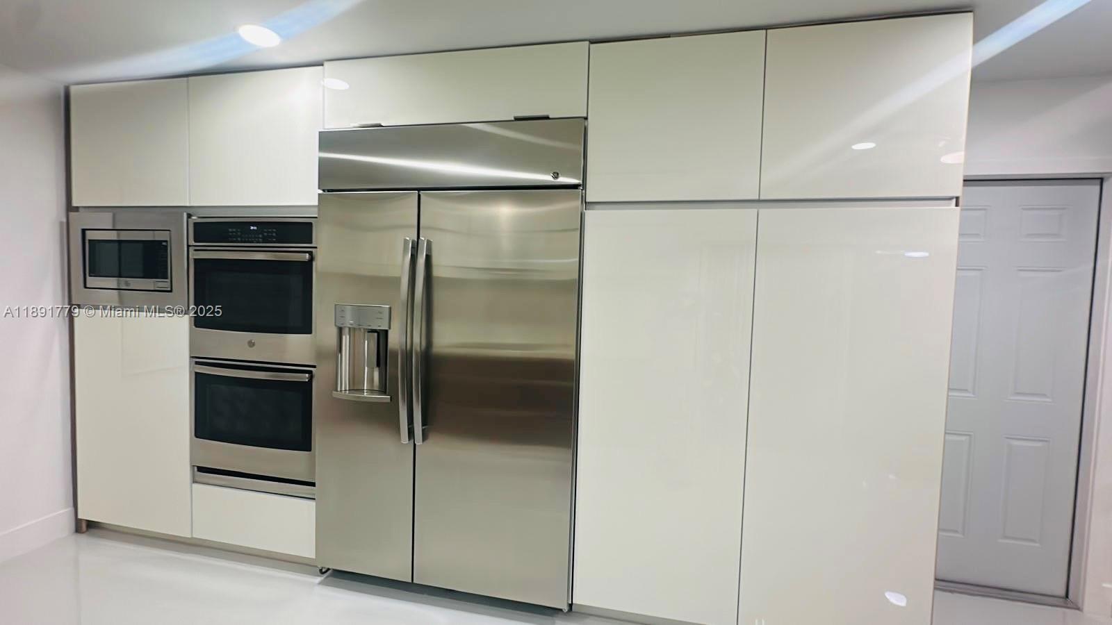 A modern kitchen features white glossy cabinetry, a stainless steel refrigerator, and built-in wall ovens — 541 SE 17th Ave # 541, Deerfield Beach FL 33441, DEERFIELD BEACH, FL