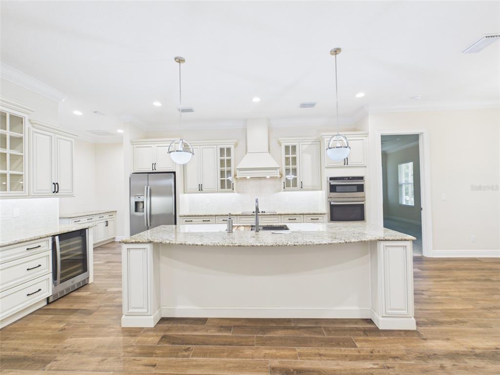 A kitchen with white cabinetry, a granite-topped island, stainless steel appliances, and wood-look flooring — 7695 SW 188 AVENUE, DUNNELLON, FL