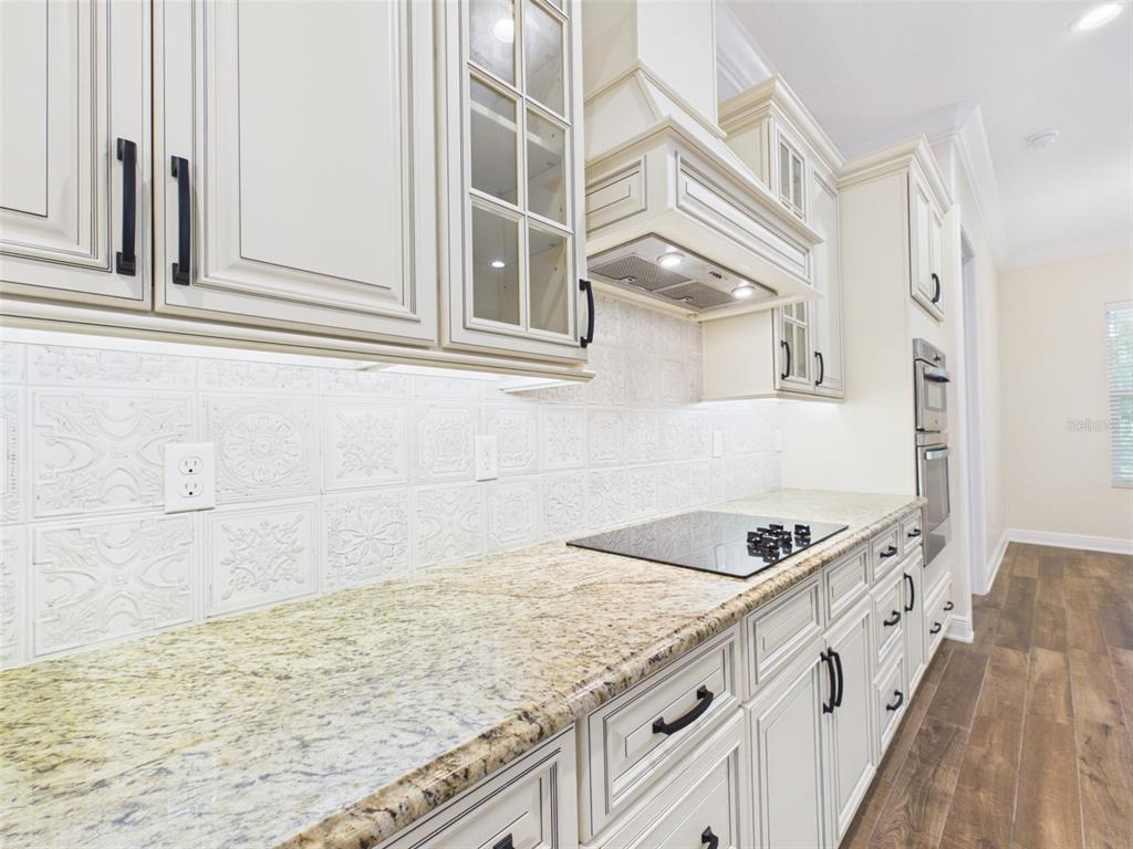 A kitchen features cream-colored cabinets, granite countertops, and a white patterned tile backsplash — 7695 SW 188 AVENUE, DUNNELLON, FL