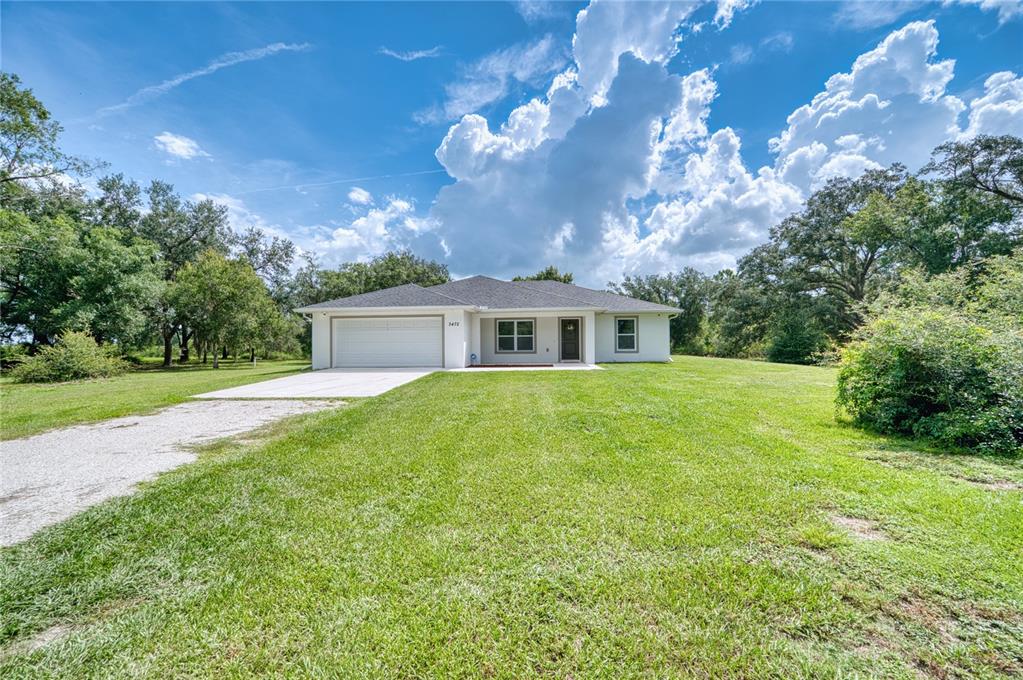 A single-story house with a white exterior, a two-car garage, and a large grassy yard — 3472 NE DAVIS STREET, ARCADIA, FL