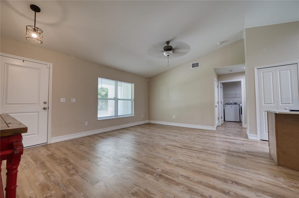 An empty living room features light-colored walls, wood-look flooring, a ceiling fan, and a window — 3472 NE DAVIS STREET, ARCADIA, FL