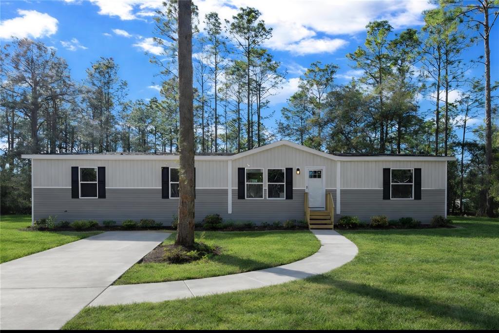 A single-story manufactured home with two-tone siding, black shutters, and a concrete walkway — 4165 SW 168TH CIRCLE, OCALA, FL