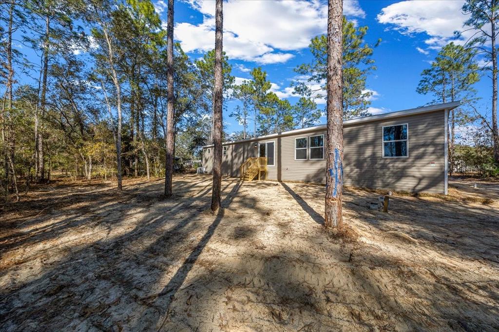 A tan manufactured home sits on a sandy lot surrounded by tall pine trees — 4165 SW 168TH CIRCLE, OCALA, FL