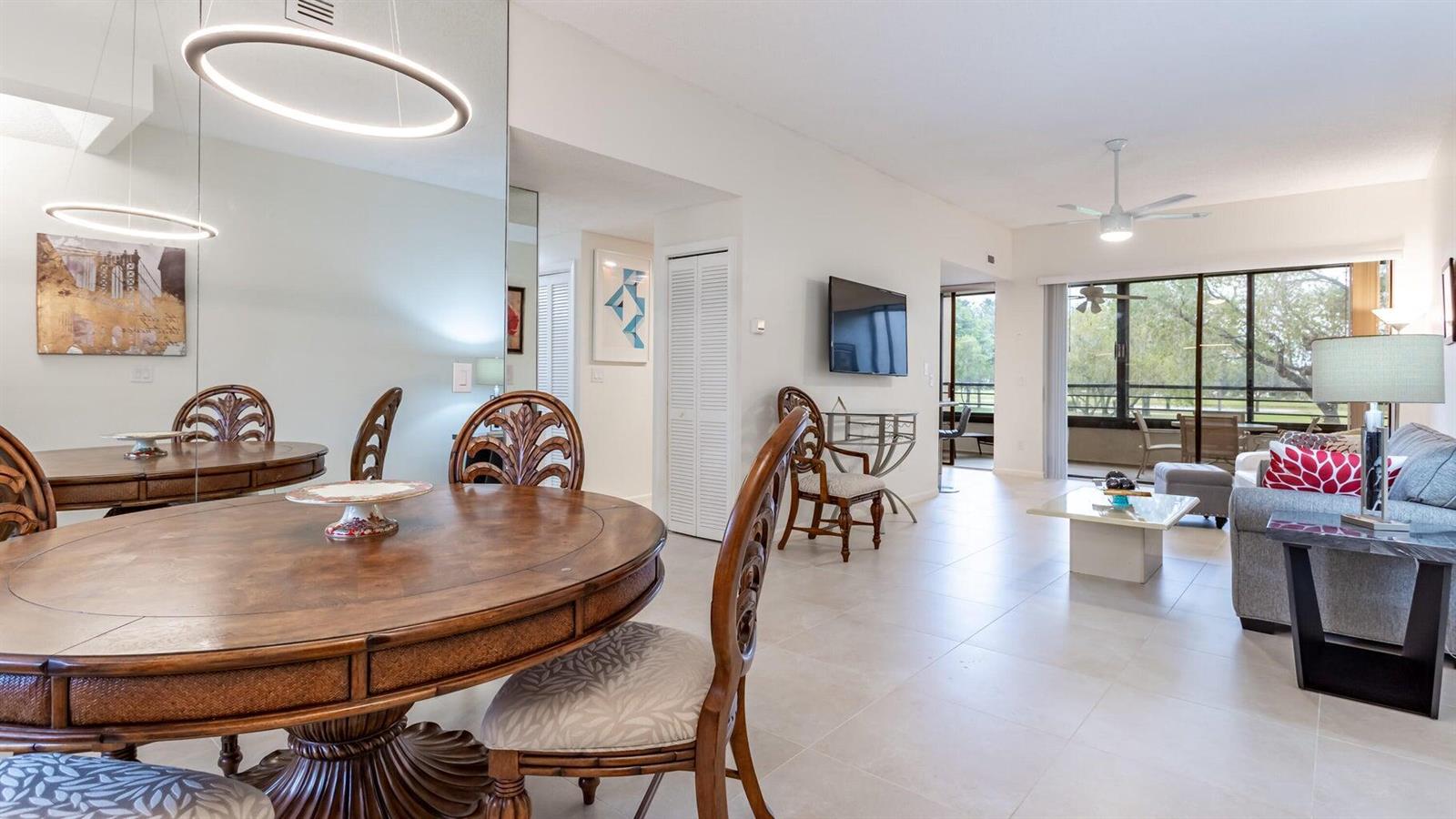 A dining area with a round wooden table leads into a living room with balcony access — 7460 La Paz Boulevard # 208, Boca Raton FL 33433, BOCA RATON, FL