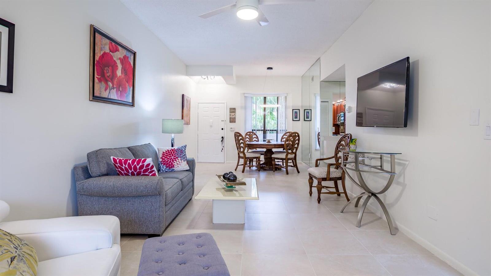 A living and dining area features a grey sofa, glass coffee table, and wooden dining set — 7460 La Paz Boulevard # 208, Boca Raton FL 33433, BOCA RATON, FL