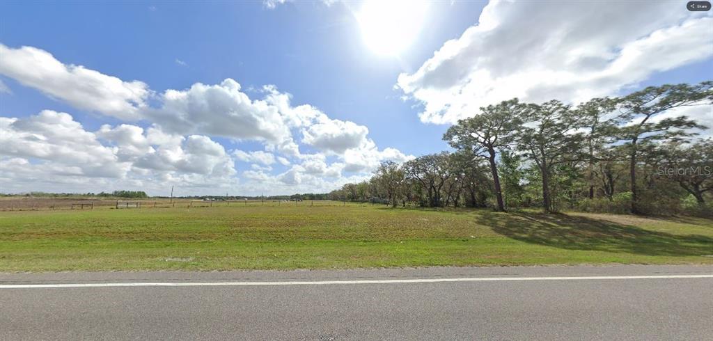 A wide, grassy vacant lot sits beside a paved road under a bright, cloudy sky — COMMONWEALTH AVE N, POLK CITY, FL
