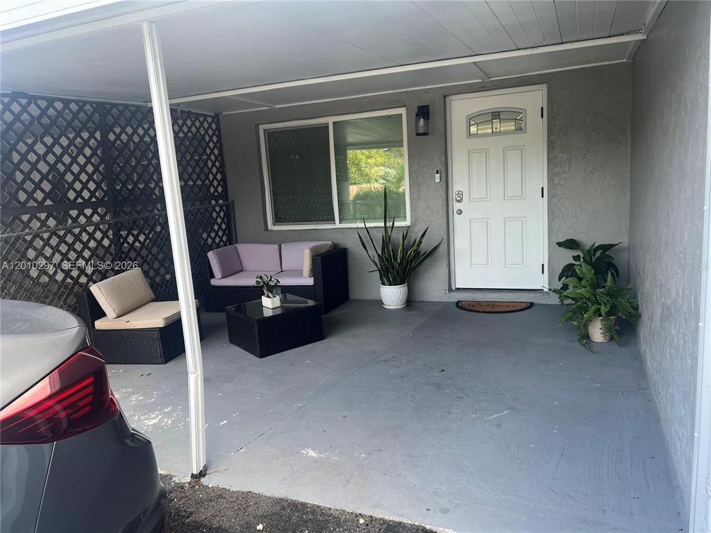 A covered carport area features a white front door, a window, and outdoor patio furniture — 6742 SW 18 COURT UNIT 2, NORTH LAUDERDALE, FL