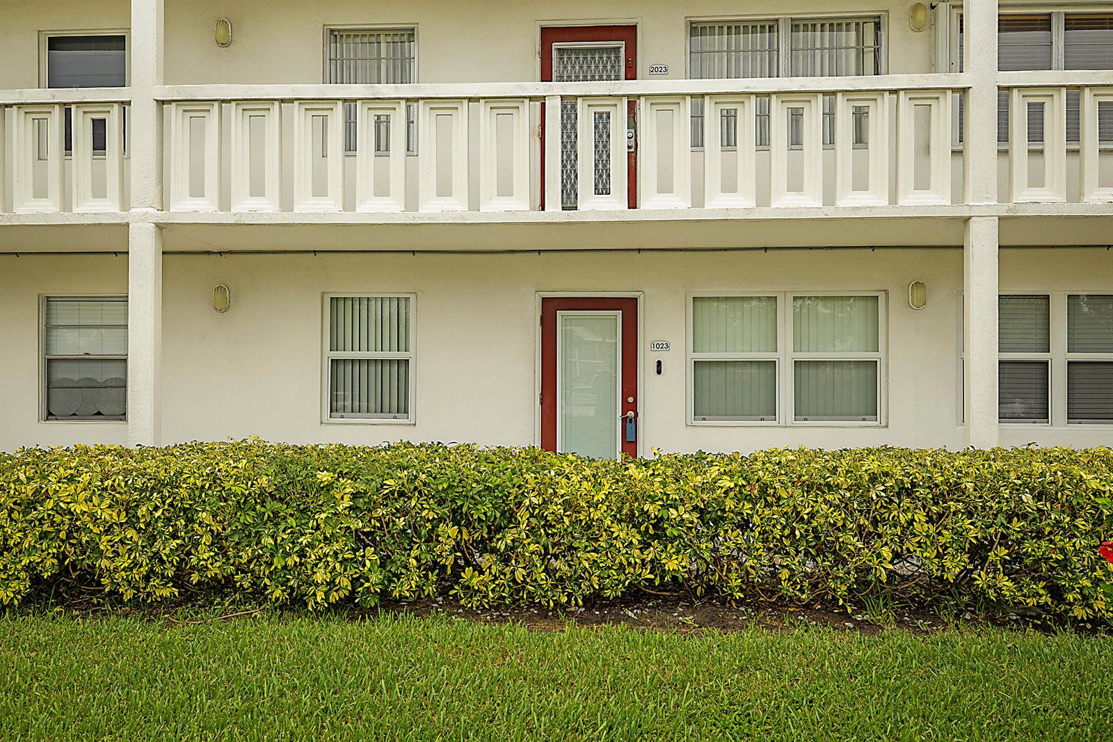 A two-story apartment building exterior features a hedge, lawn, and red-framed entry doors — 1023 Ellesmere B, Deerfield Beach FL 33442, DEERFIELD BEACH, FL