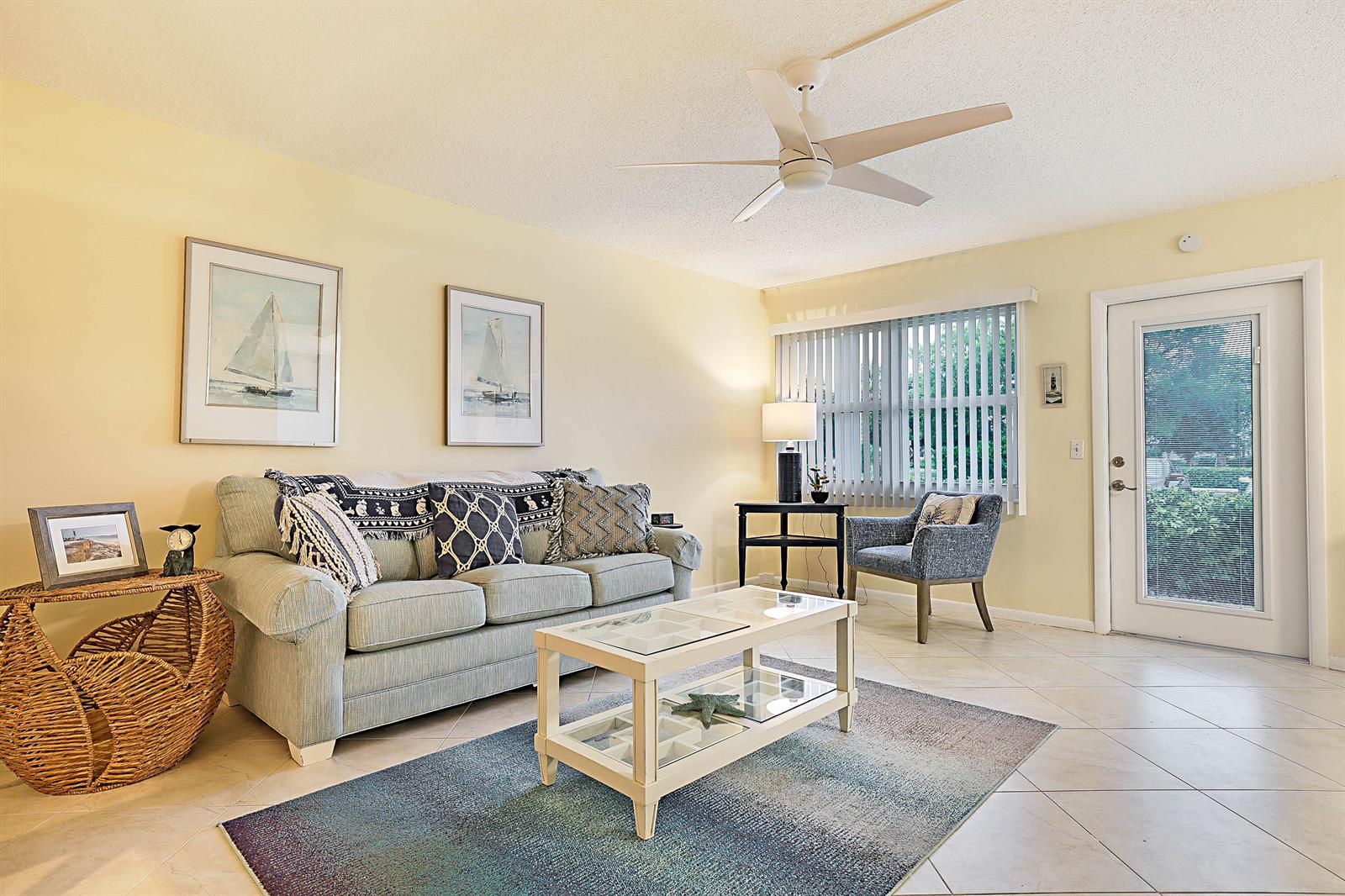 A living room features a light blue sofa, glass coffee table, area rug, and tile flooring — 1023 Ellesmere B, Deerfield Beach FL 33442, DEERFIELD BEACH, FL