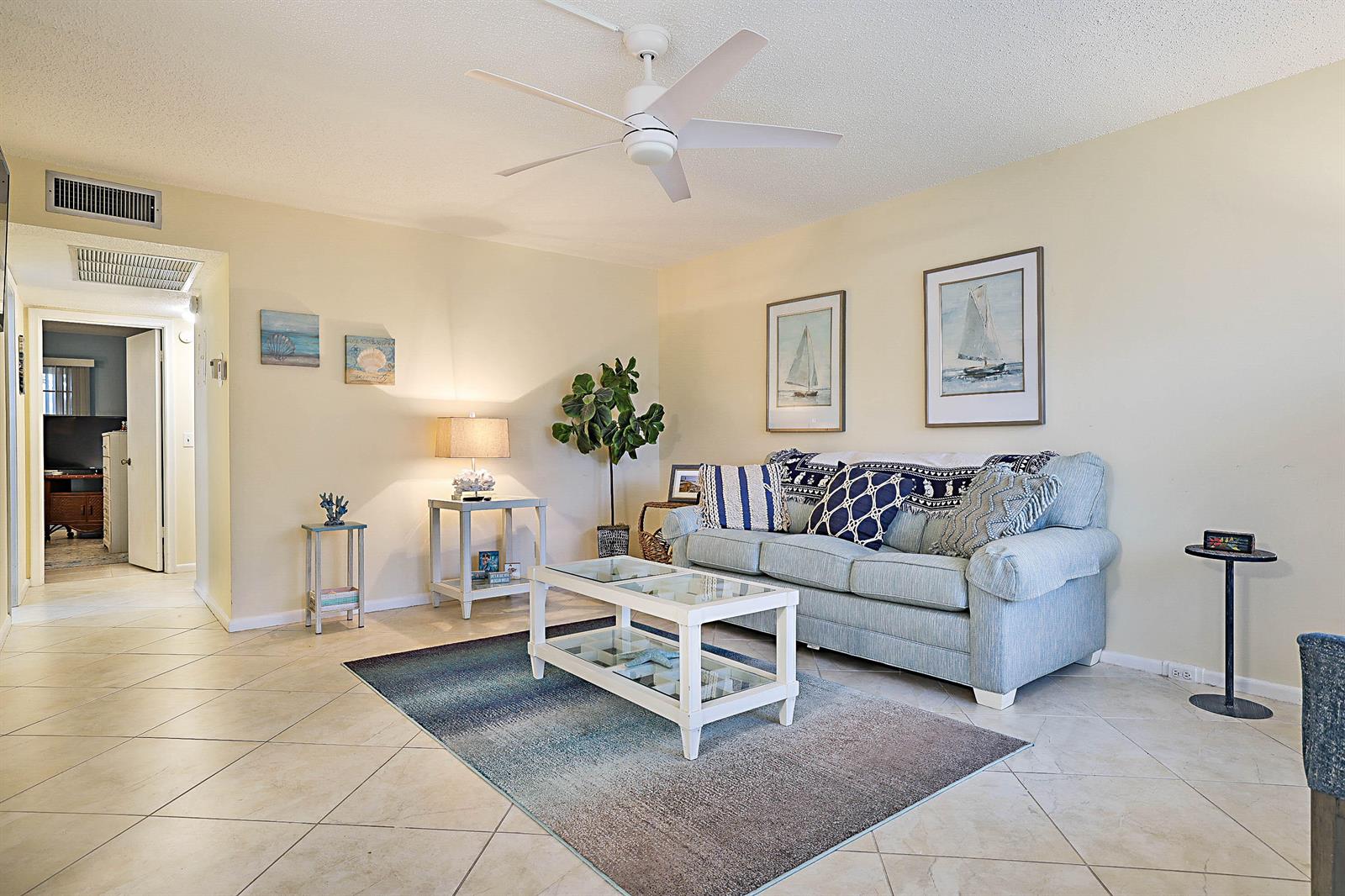 A living room features a light blue sofa, a glass coffee table, and tile flooring — 1023 Ellesmere B, Deerfield Beach FL 33442, DEERFIELD BEACH, FL
