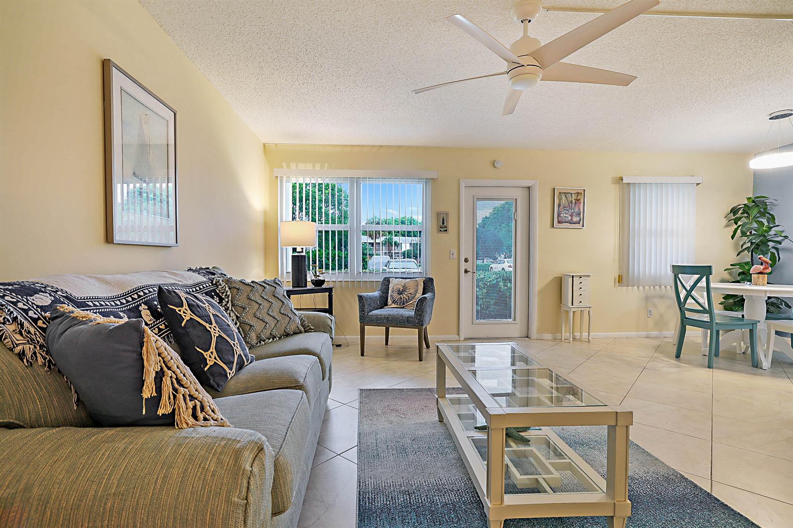 A living room with a sofa, glass coffee table, dining area, and a ceiling fan — 1023 Ellesmere B, Deerfield Beach FL 33442, DEERFIELD BEACH, FL