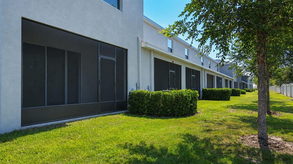 A row of townhouses features screened-in patios, manicured hedges, and a grassy lawn — 5311 DRAGONFLY DRIVE, WILDWOOD, FL