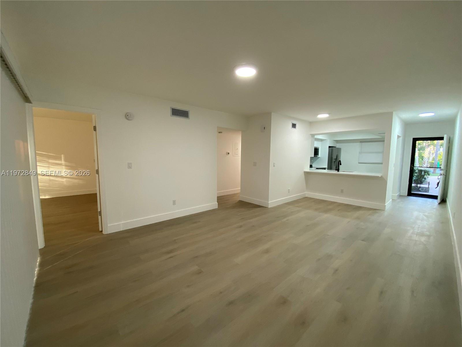 An open living area features light wood-look flooring, white walls, and a kitchen pass-through window — 1765 Courtyard way # 103, Naples FL 33114, NAPLES, FL