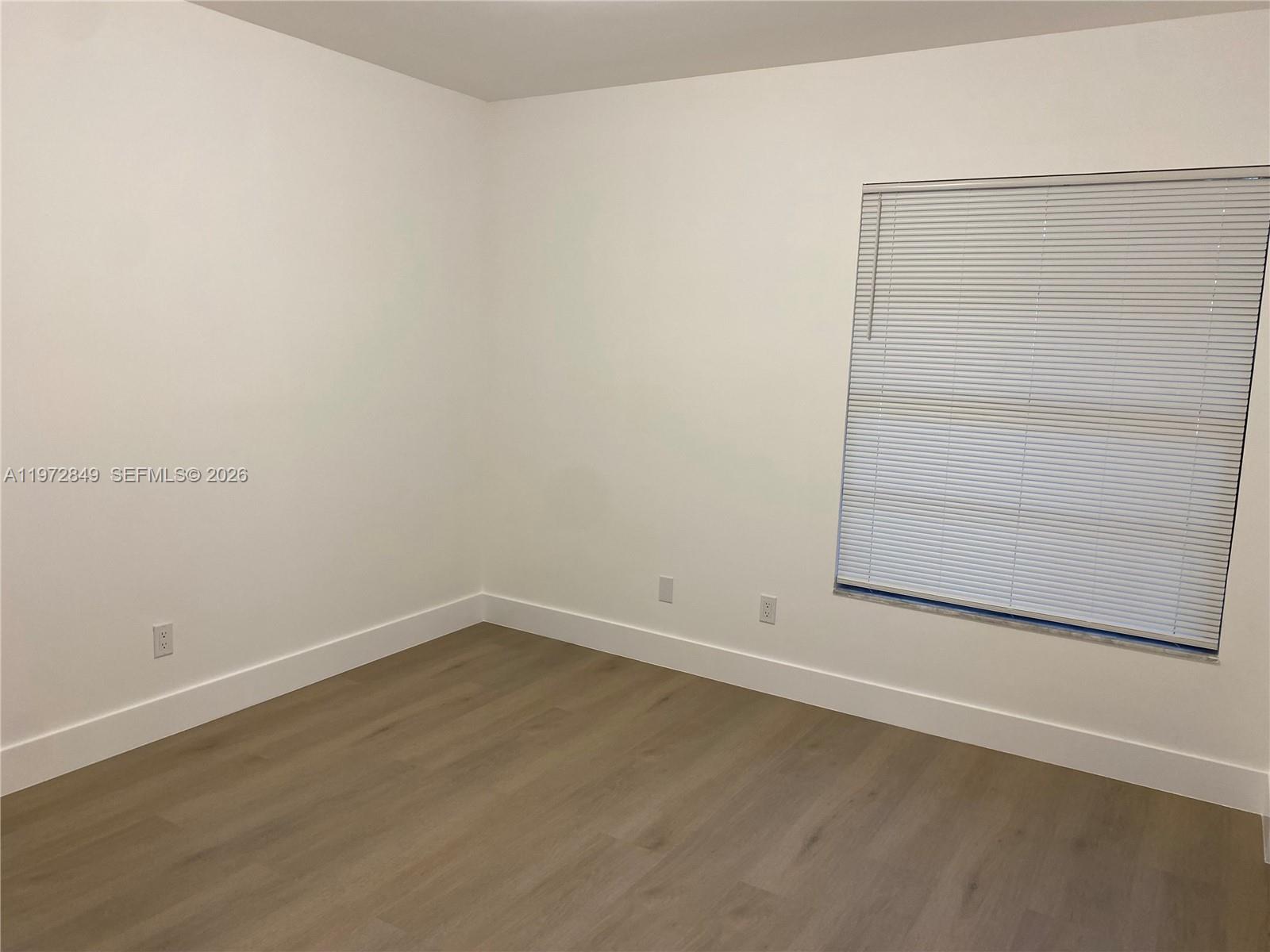 An empty bedroom features white walls, light wood-look flooring, and a window with blinds — 1765 Courtyard way # 103, Naples FL 33114, NAPLES, FL