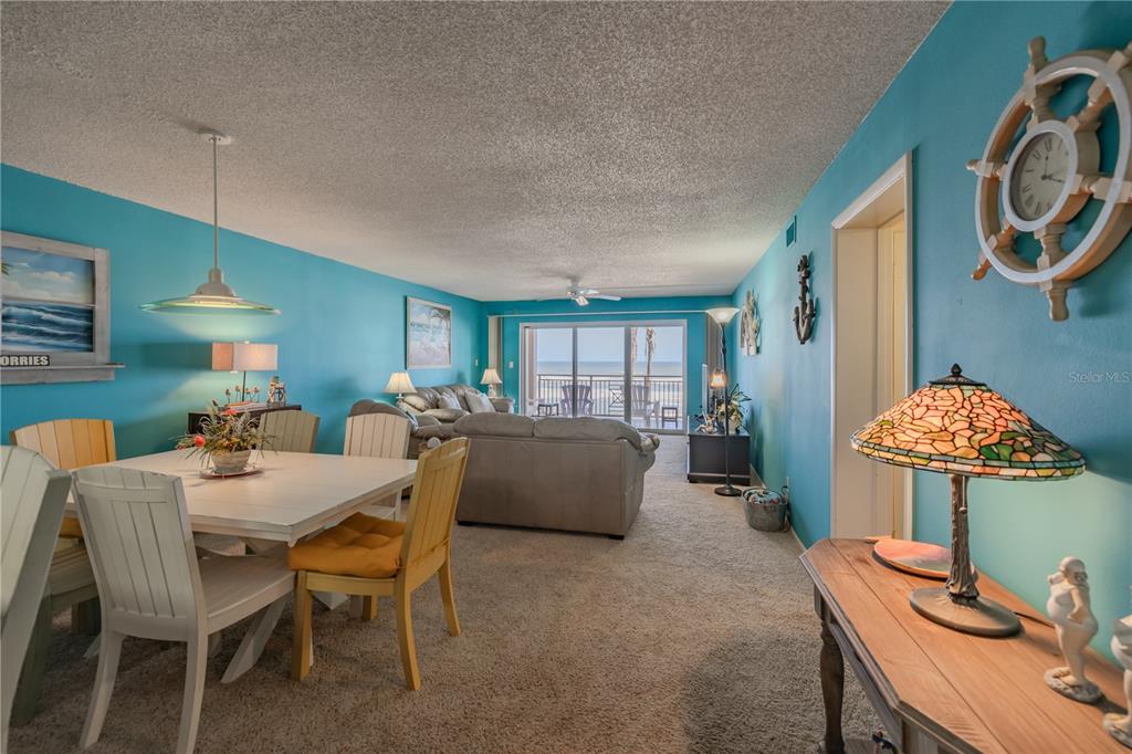 A dining area and living room with blue walls, carpeted floors, and a balcony view — 5501 S ATLANTIC AVENUE UNIT 3070, NEW SMYRNA BEACH, FL