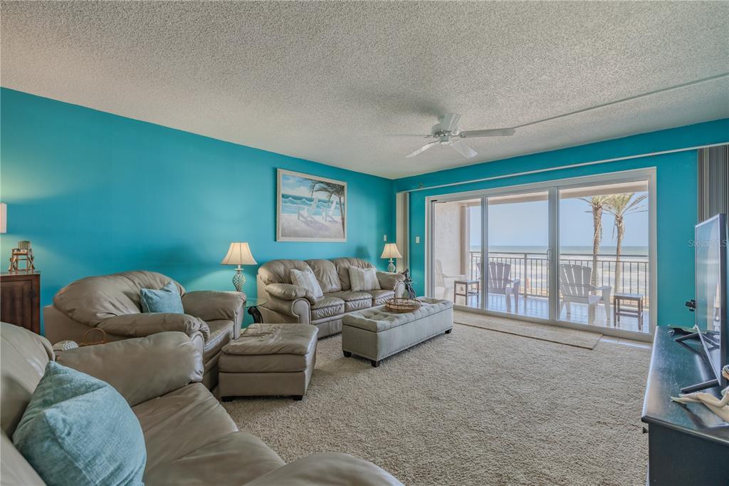 A living room with turquoise walls, beige leather furniture, and a sliding door to a balcony — 5501 S ATLANTIC AVENUE UNIT 3070, NEW SMYRNA BEACH, FL